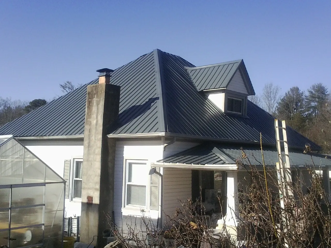 Dark blue standing seam metal roof on a white farmhouse with dormer — Slate & Tile Roof Repair by Roofing Brothers in Stella