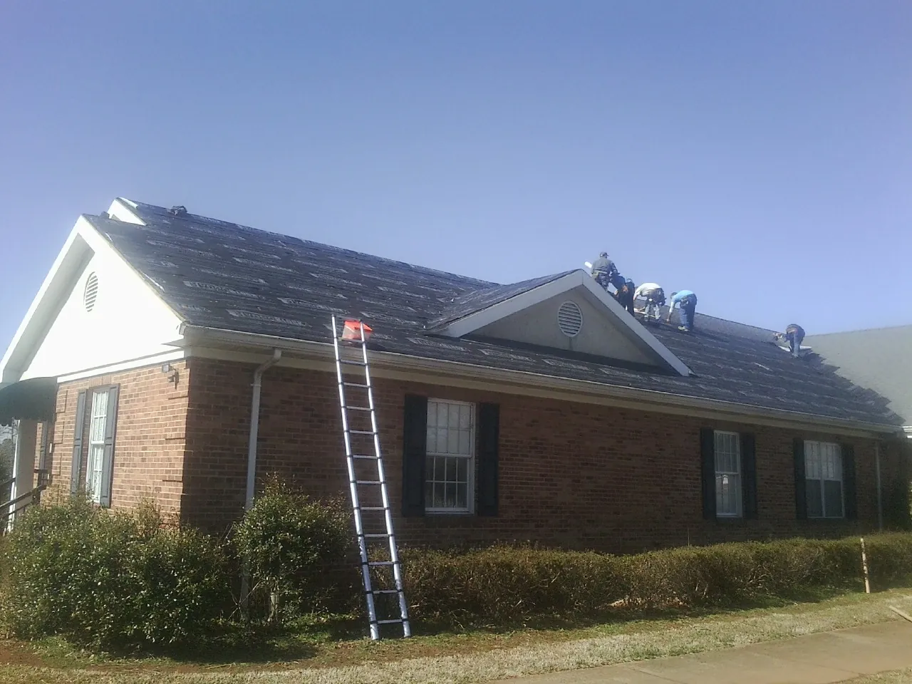 Crew tearing shingles off a brick ranch roof with a ladder set — Emergency Roof Repair work by our crew in Stella