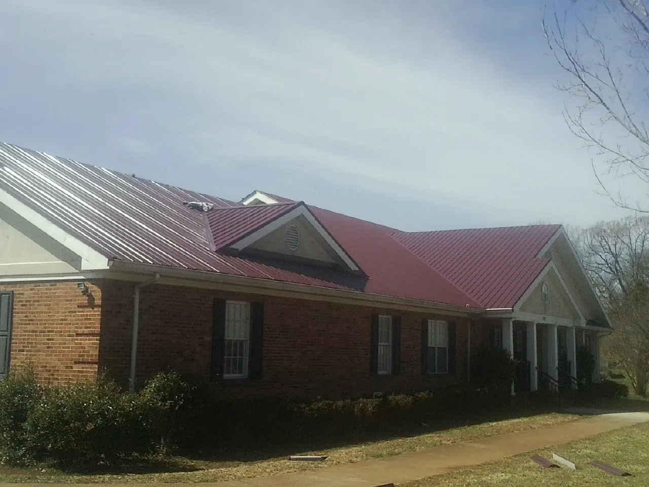 Red metal roof with gabled entries on a long brick building, from a Hail Damage Roof Repair job in Stella