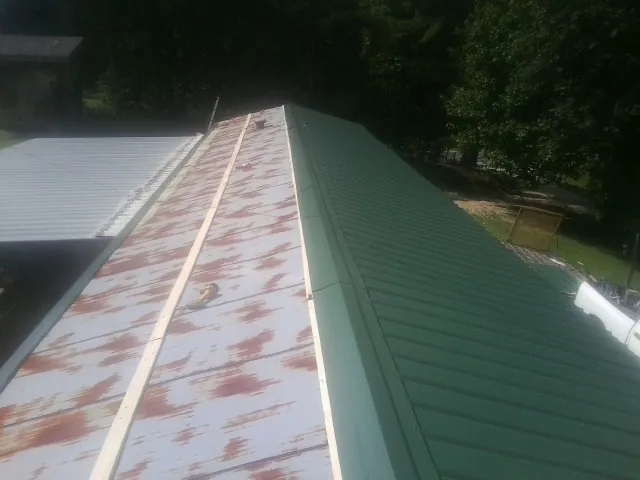 Old rusted panels beside newly installed green metal roofing — Wind Damage Roof Repair by Roofing Brothers in Stella
