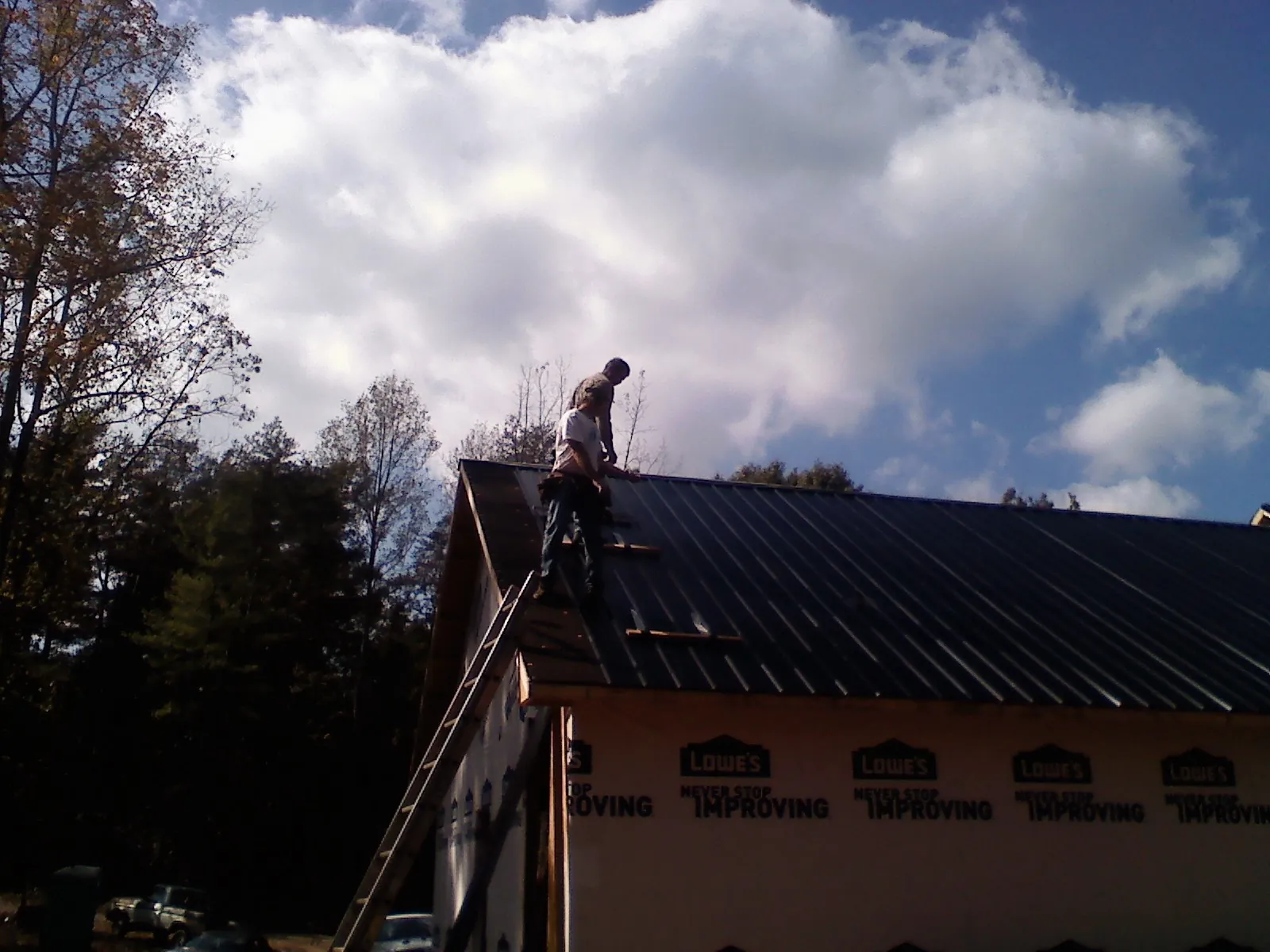 Roofer fastening dark metal panels high against a cloudy sky, from a Roof Inspection job in Stella