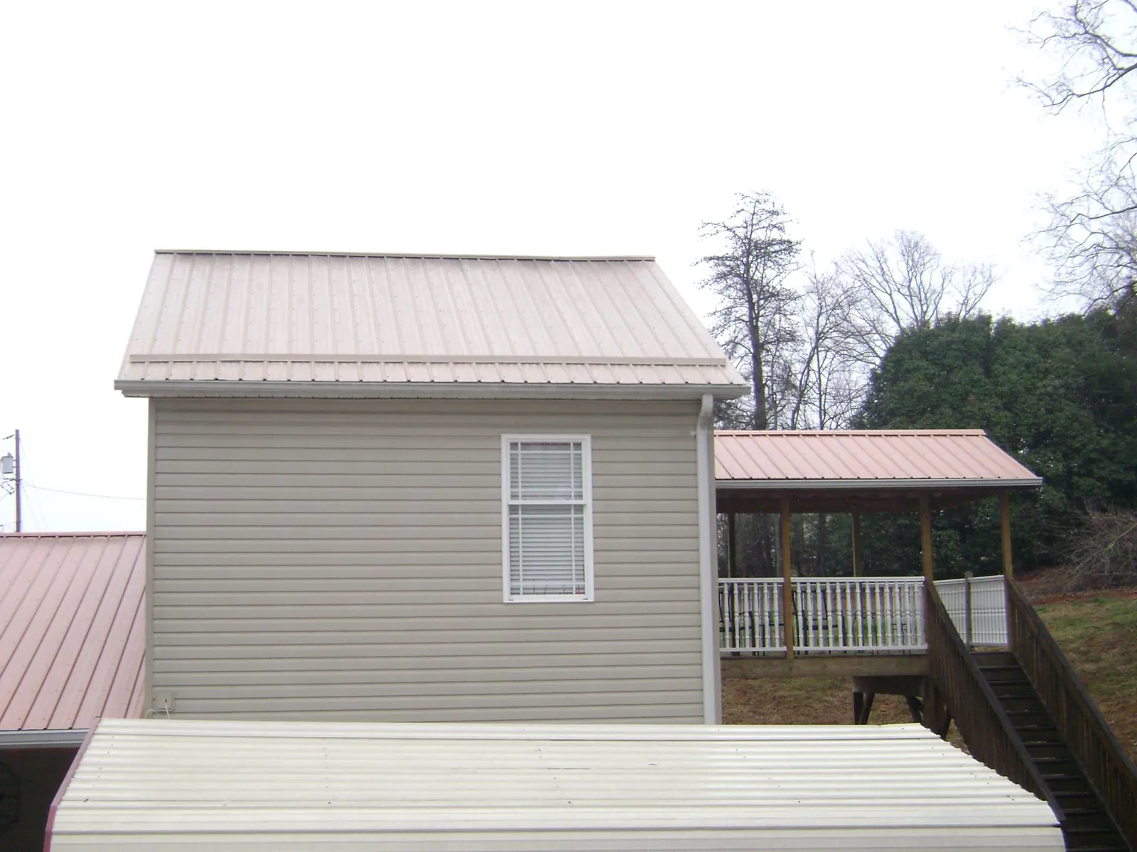 Tan metal roofs on a two story addition and attached porch, from a Roof Replacement job in Stella